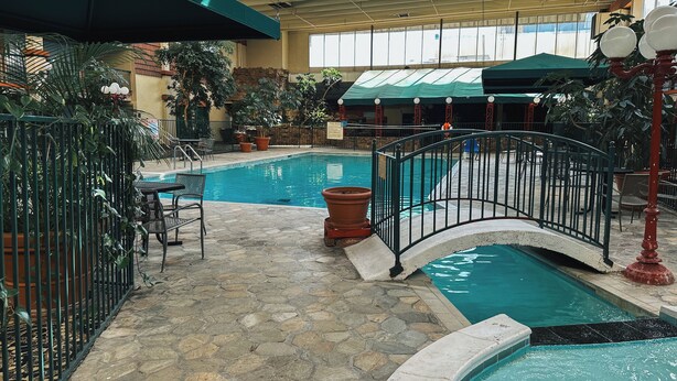 An indoor pool area with a stone floor, a small bridge, and a seating area with chairs and tables. - Clarion Inn (Fort Collins)