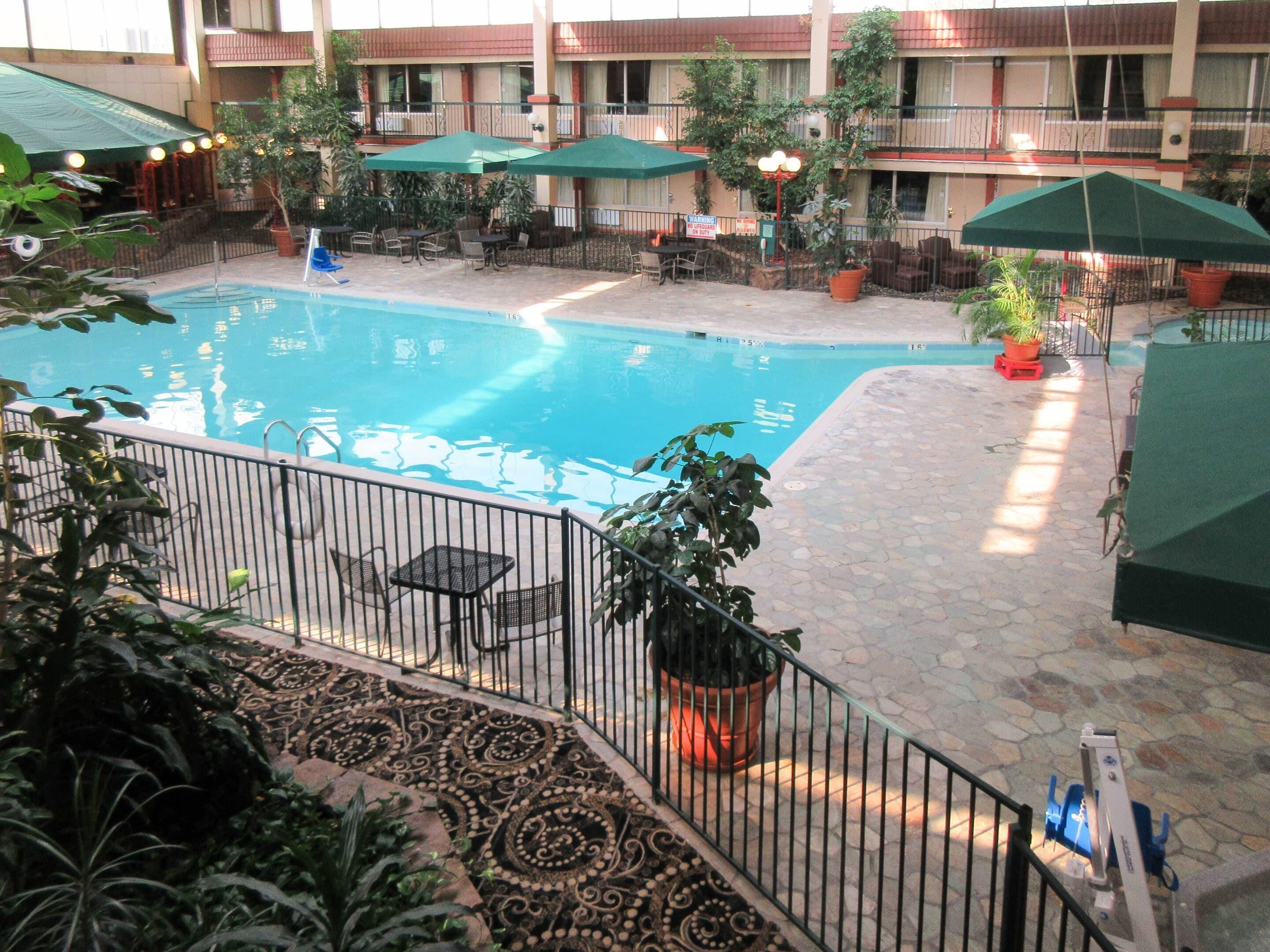 A hotel pool area with a stone floor, surrounded by outdoor seating and umbrellas.