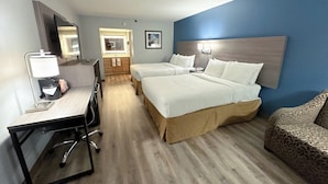 A hotel room with a desk, two beds, a chair, a bathroom, and a blue accent wall. - Clarion Inn (Fort Collins)