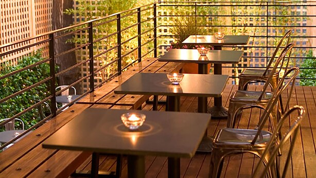 An outdoor patio with tables and chairs, string lights, and a wooden deck.