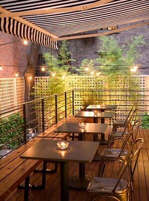 An outdoor patio with tables and chairs, string lights, and a wooden deck.