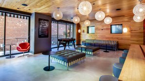 A modern interior with wooden ceiling, round hanging lights, a red chair, a sofa, and a ping pong table.