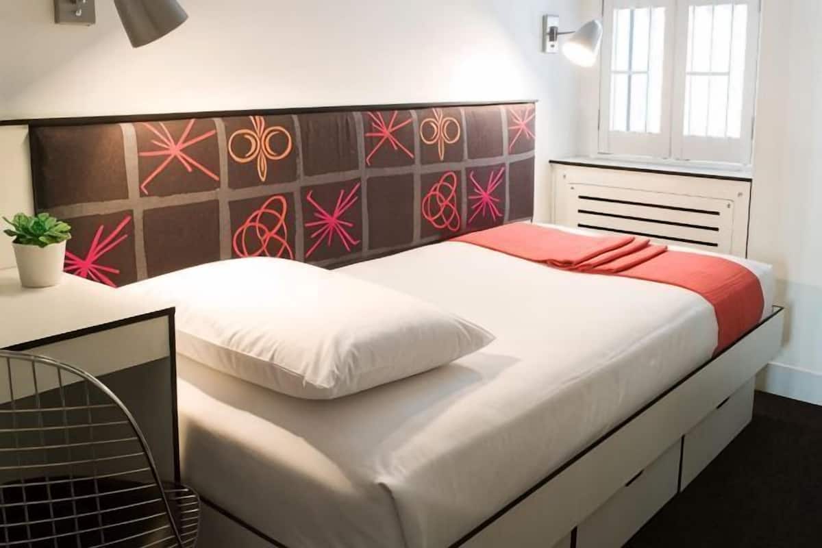 A bed with a white and red bedspread, a white pillow, and a decorative headboard with geometric patterns.