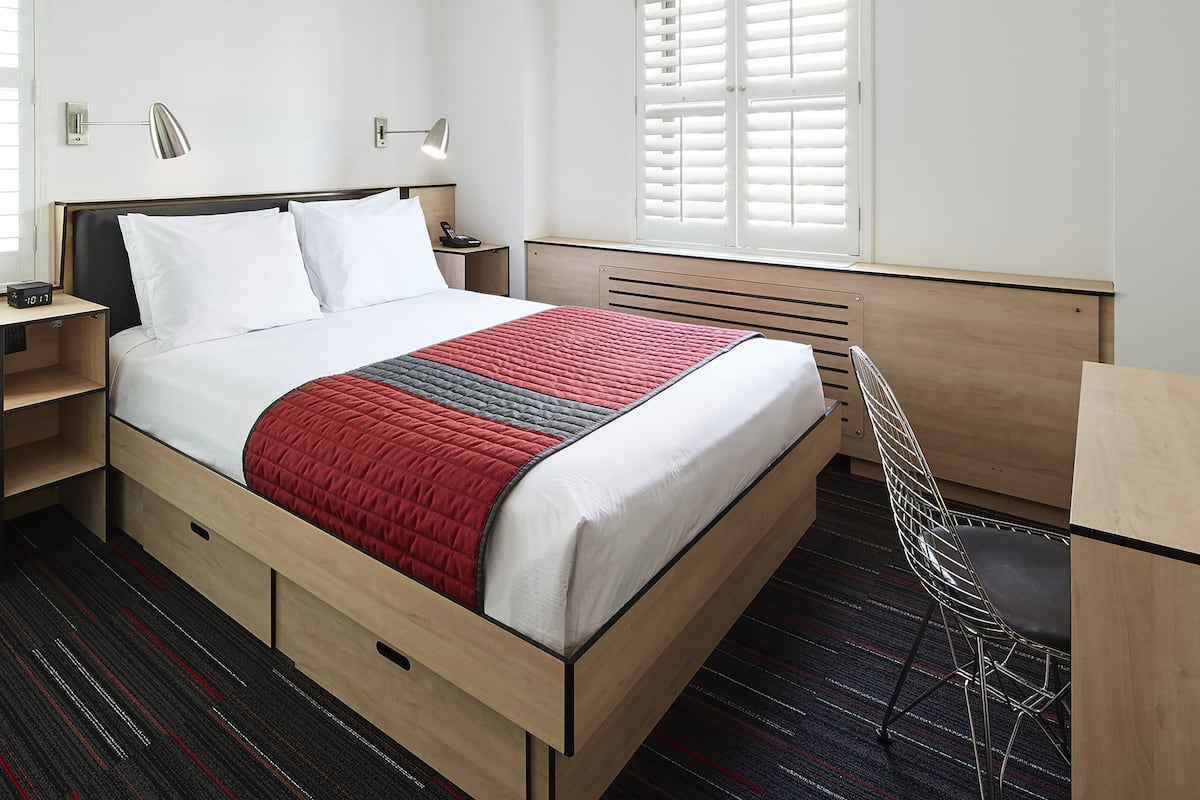 A modern hotel room with a neatly made bed, bedside tables, a desk, and a chair.
