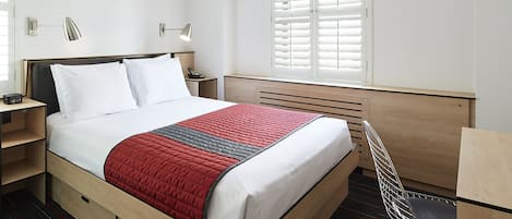 Quarto de hotel moderno com uma cama bem arrumada, mesas de cabeceira, escrivaninha e uma cadeira.