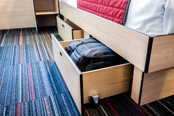 A hotel room with a wooden bed, a drawer with a black bag, and a striped carpet.