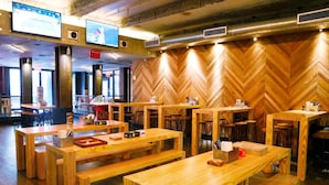 A restaurant with wooden tables and benches, a herringbone-patterned wall, and multiple screens on the ceiling.