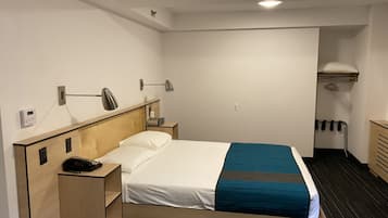 Een hotelkamer met een bed, nachtkastje, lamp en een klein bureau met telefoon.