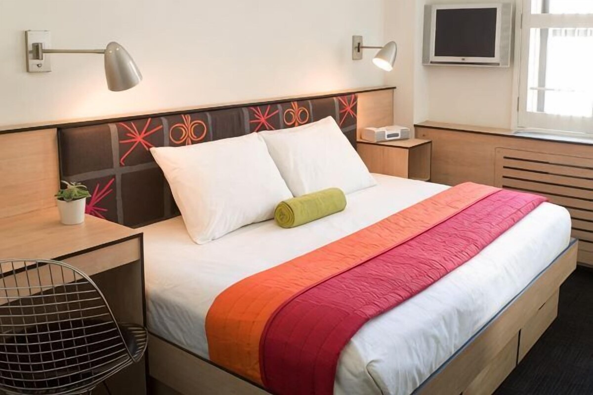 Une chambre d’hôtel avec un lit, des tables de chevet, une chaise, un téléviseur et une fenêtre.