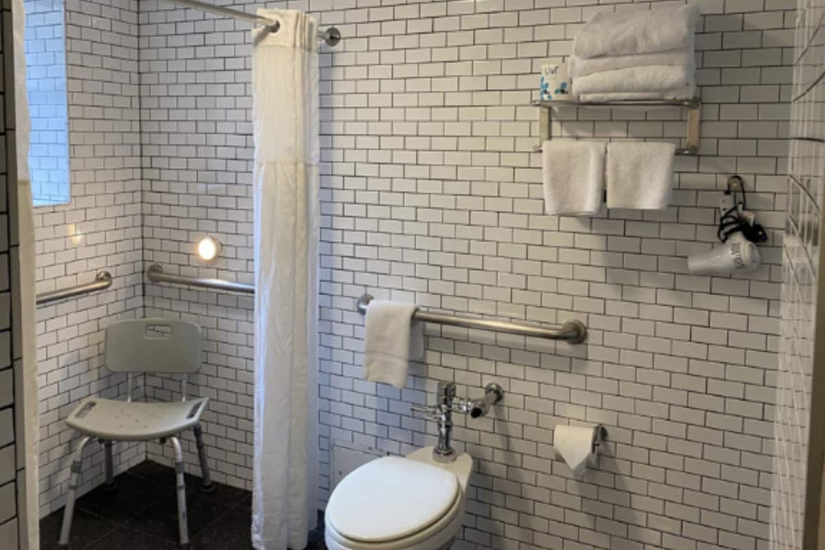 A bathroom with white brick walls, a white toilet, a white sink, a white shower chair, and a white towel rack.