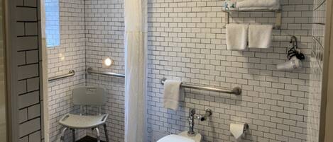 A bathroom with white brick walls, a white toilet, a white sink, a white shower chair, and a white towel rack.