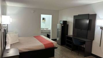 A hotel room with a bed, a desk, a TV, and a refrigerator.