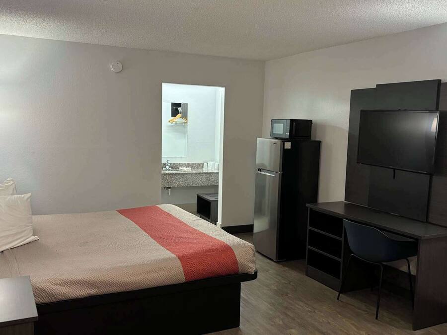 A hotel room with a bed, a desk, a TV, and a refrigerator.