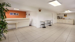 A spacious kitchen with white cabinets, a dining area with metal chairs, and a counter with a plant. - Motel 6 Macclenny, FL (MacClenny)