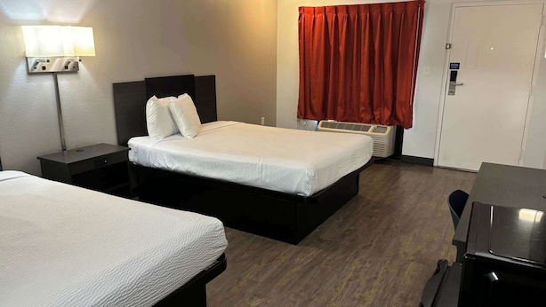 A hotel room with two beds, a desk, a lamp, a heater, and a door. - Motel 6 Macclenny, FL (MacClenny)