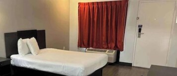 Habitación de hotel con cama, mesita de noche, cortina roja y una puerta.