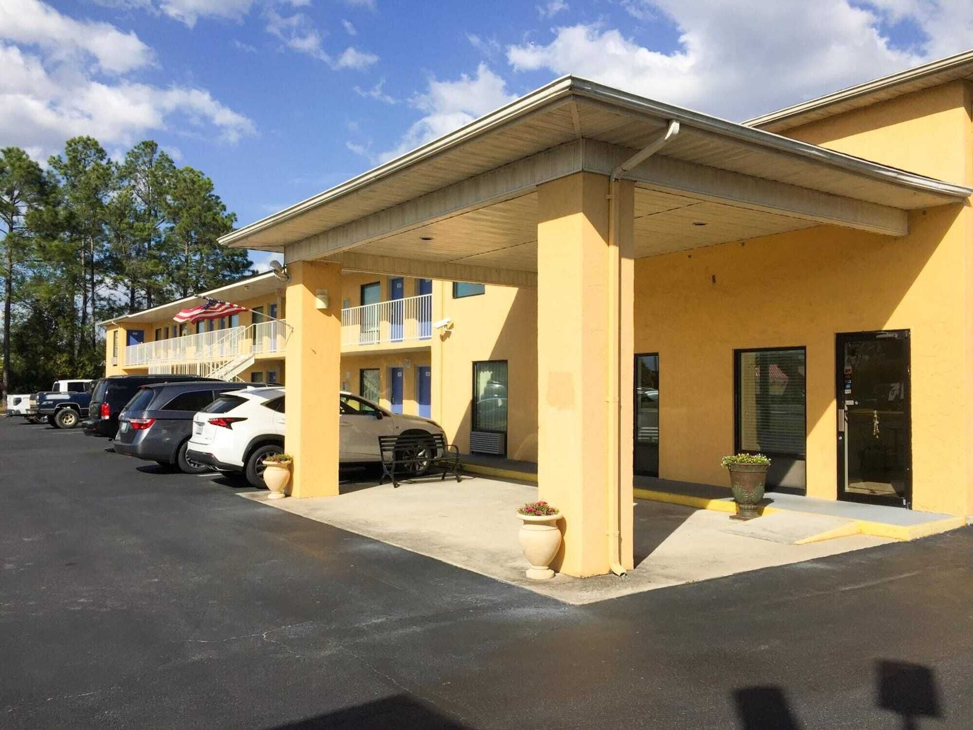 A motel with a covered parking area, multiple rooms with balconies, and a row of parked cars.