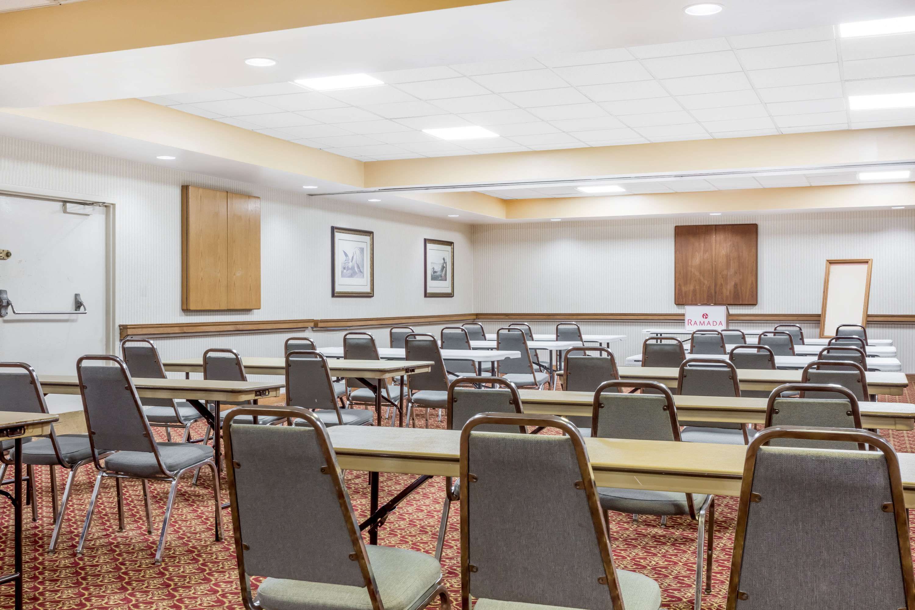 A conference room with rows of tables and chairs, a carpeted floor, and a white ceiling with recessed lighting.