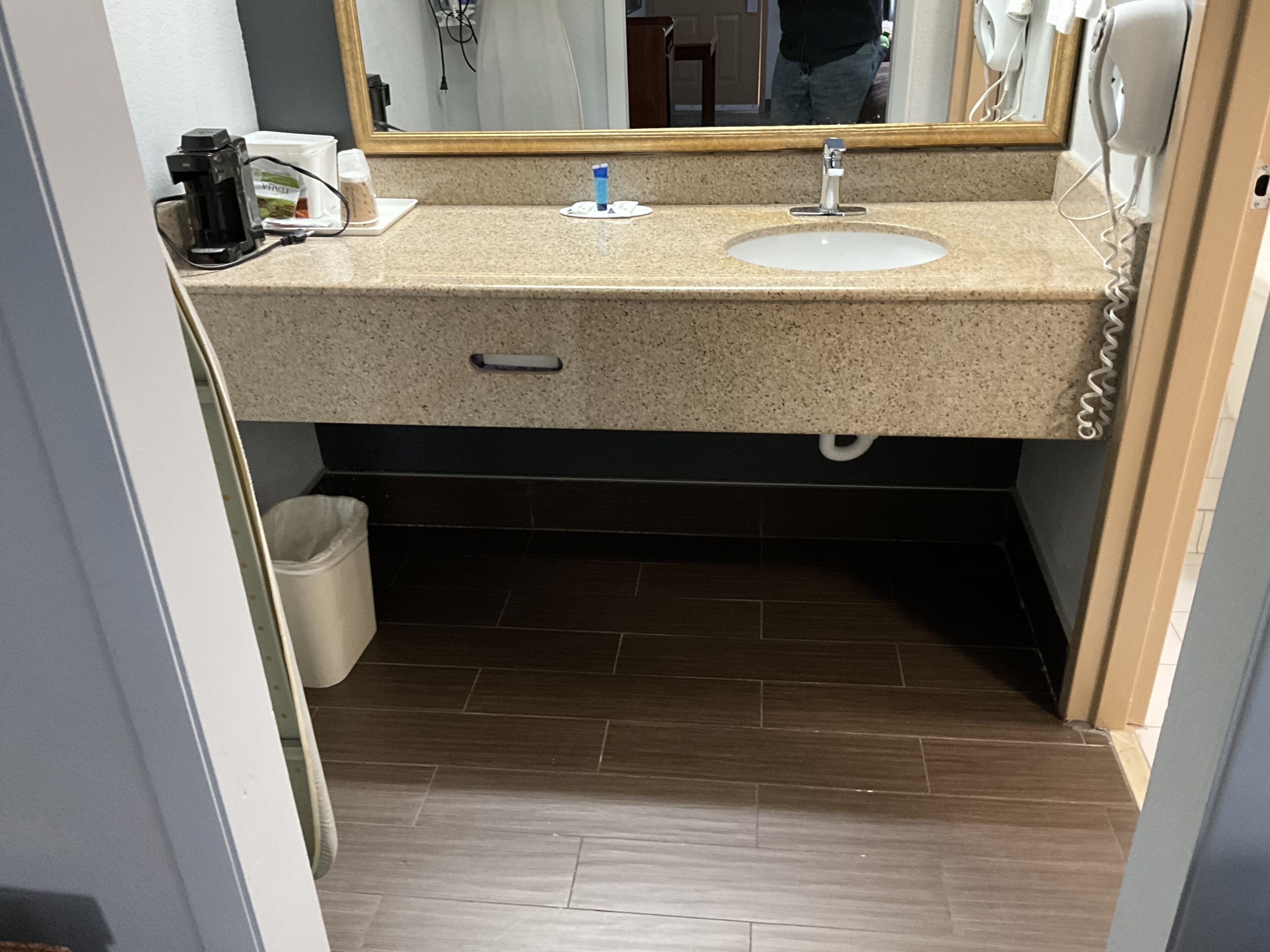 Une salle de bain avec un comptoir en granit, deux lavabos, un miroir, un sèche-cheveux et une poubelle.