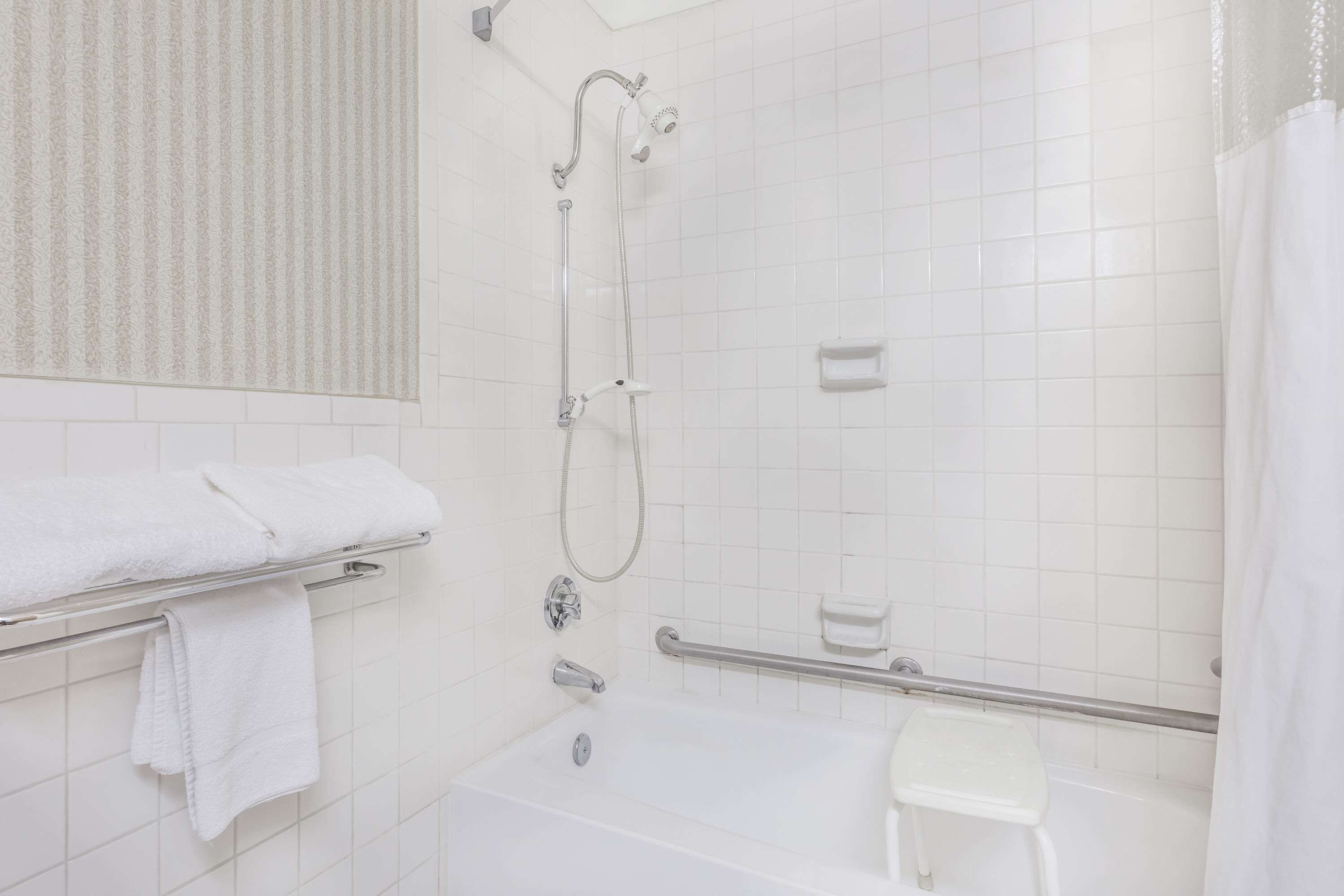 A modern bathroom with a bathtub, shower, and a small white stool.