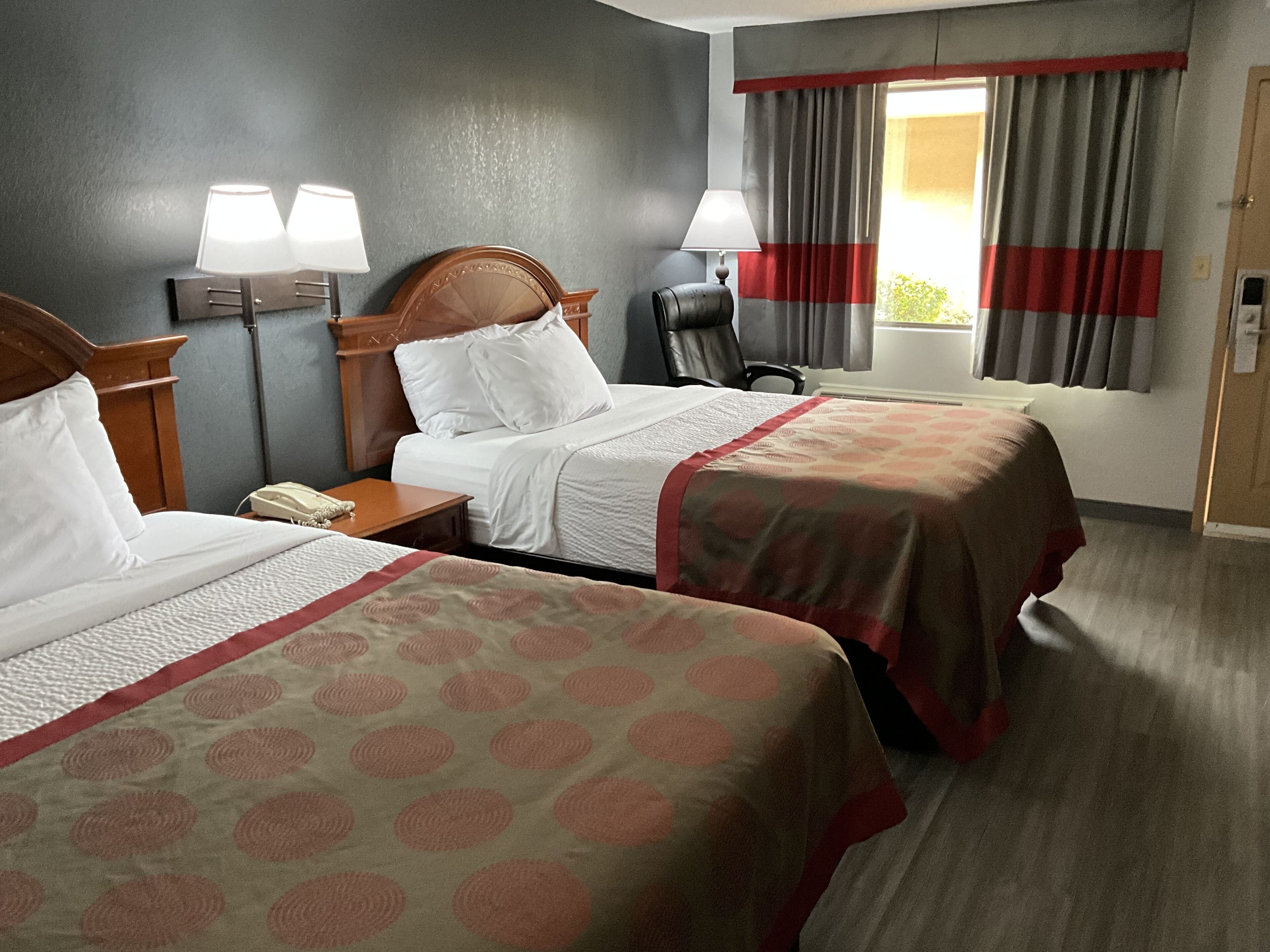 Habitació d'hotel amb dos llits, una escriptori, una cadira i una finestra amb cortines.