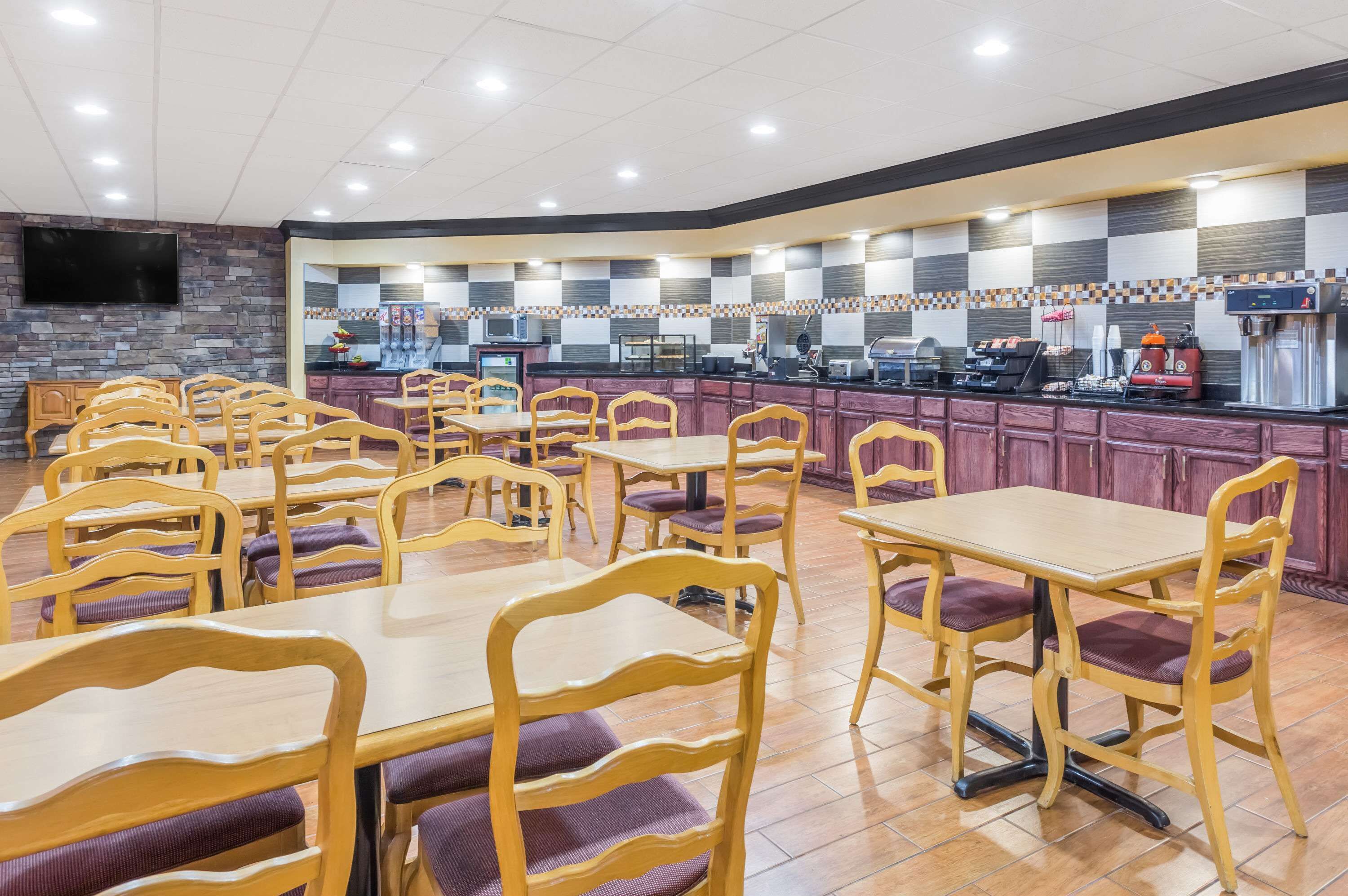Un restaurante con varias mesas y sillas, una zona de cocina con electrodomésticos y un televisor de pantalla plana montado en la pared.