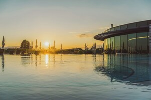 Una piscina con vistas a la puesta de sol, un edificio moderno con ventanales de vidrio y una fila de tumbonas.