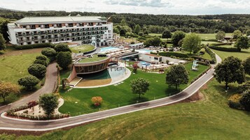 Un hotel moderno con piscina, mobiliario exterior y un campo de golf al fondo.