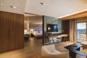 Una habitación de hotel moderna con una cama grande, un escritorio con dos sillas, un sofá y un televisor montado en una pared de piedra.