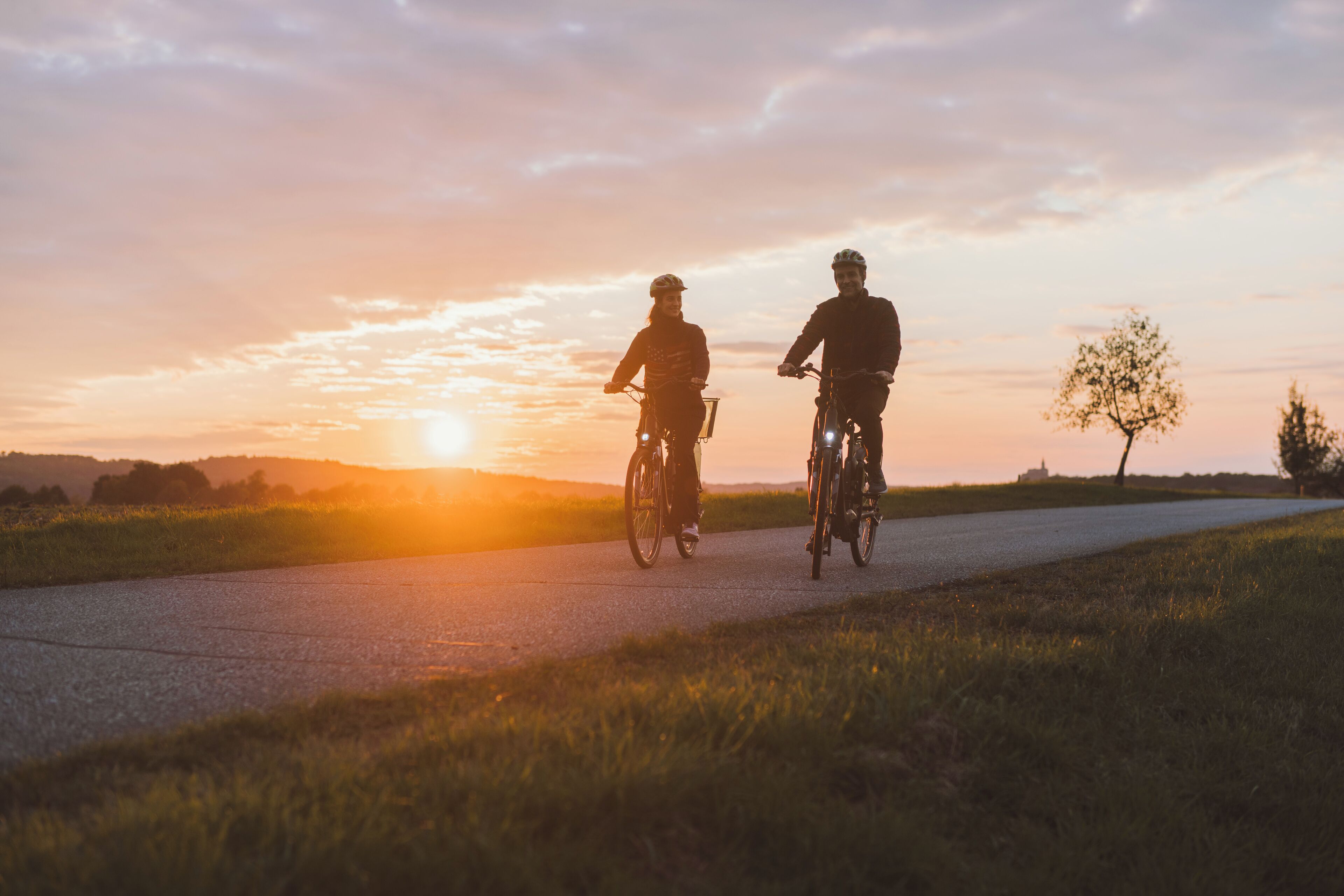Dos personas andando en bicicleta por una carretera al atardecer.