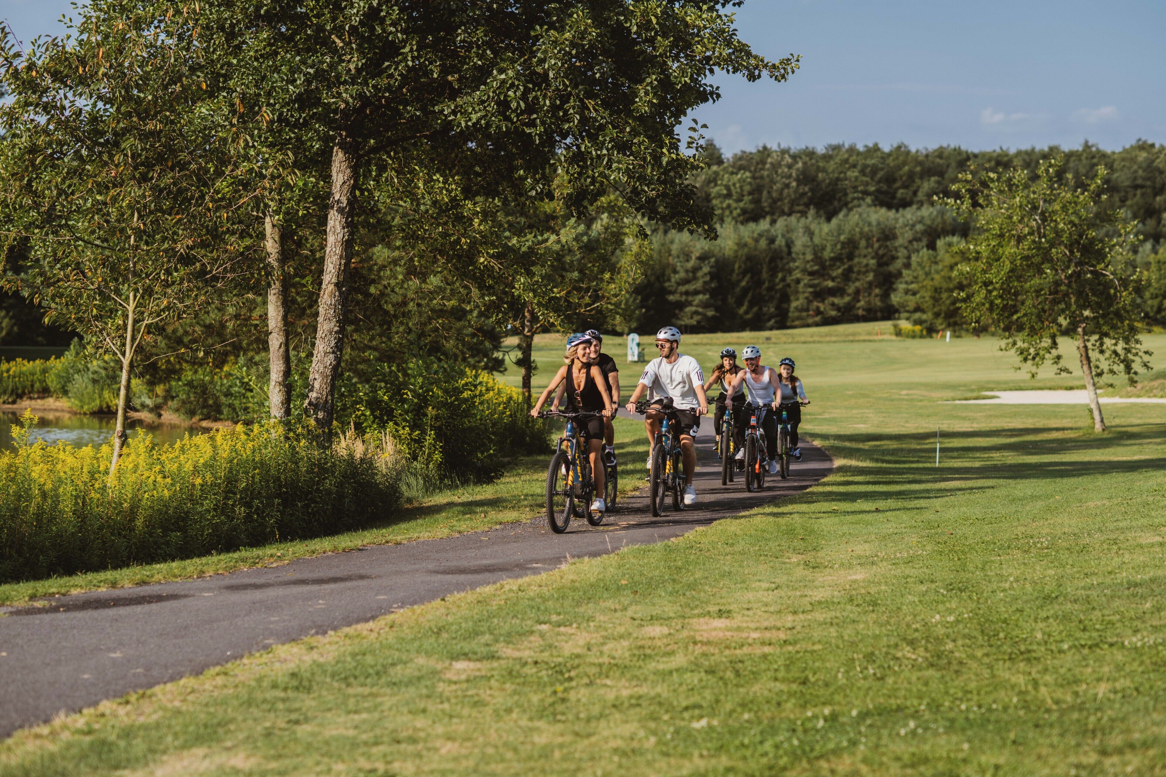 A group of cyclists on a paved path surrounded by greenery and trees.