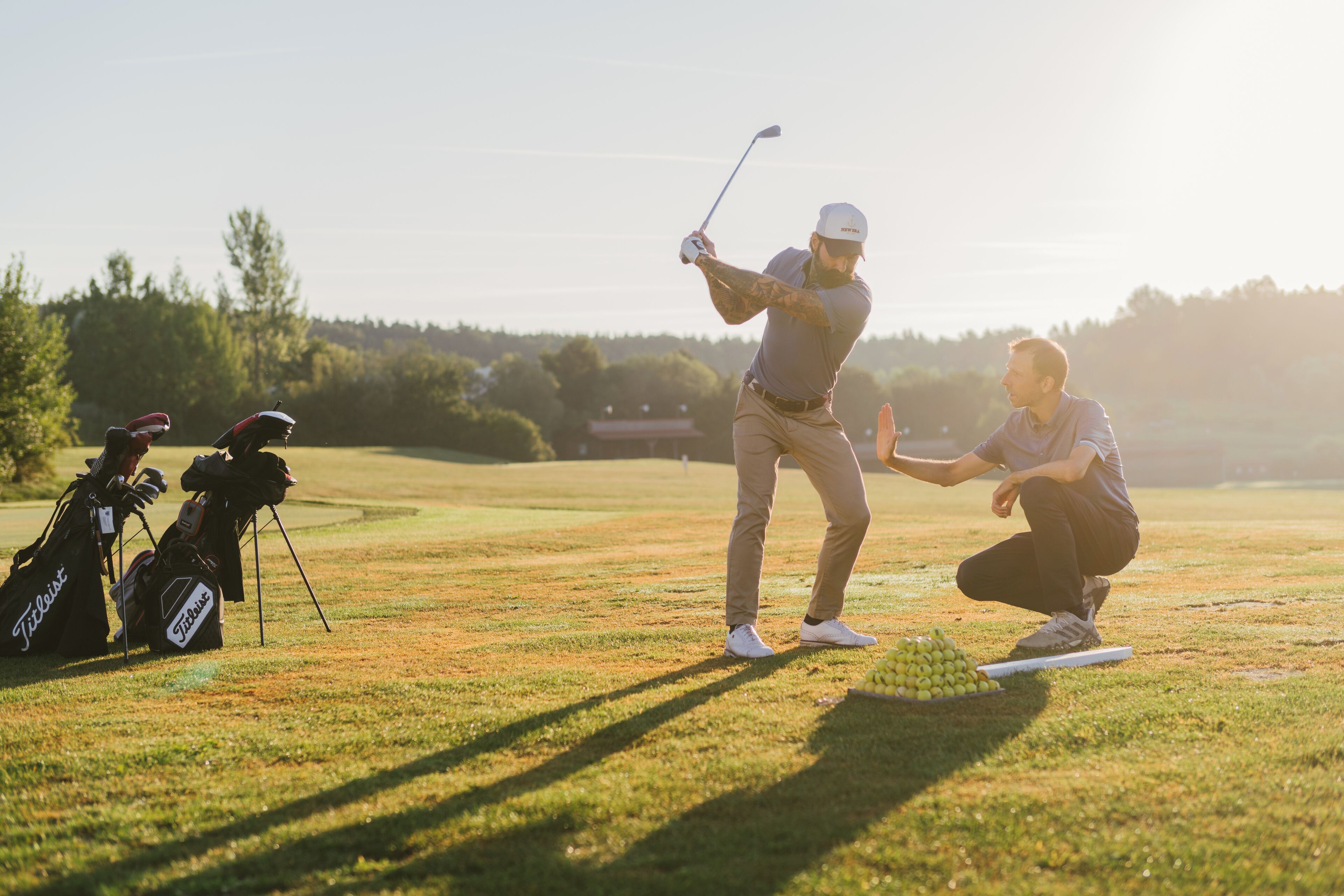 Een golfbaan met een speler die een bal staat te bereiden te slaan, golftassen en een caddie.