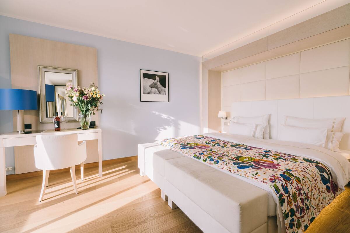 A modern hotel room with a large bed, a desk, a chair, and a mirror.
