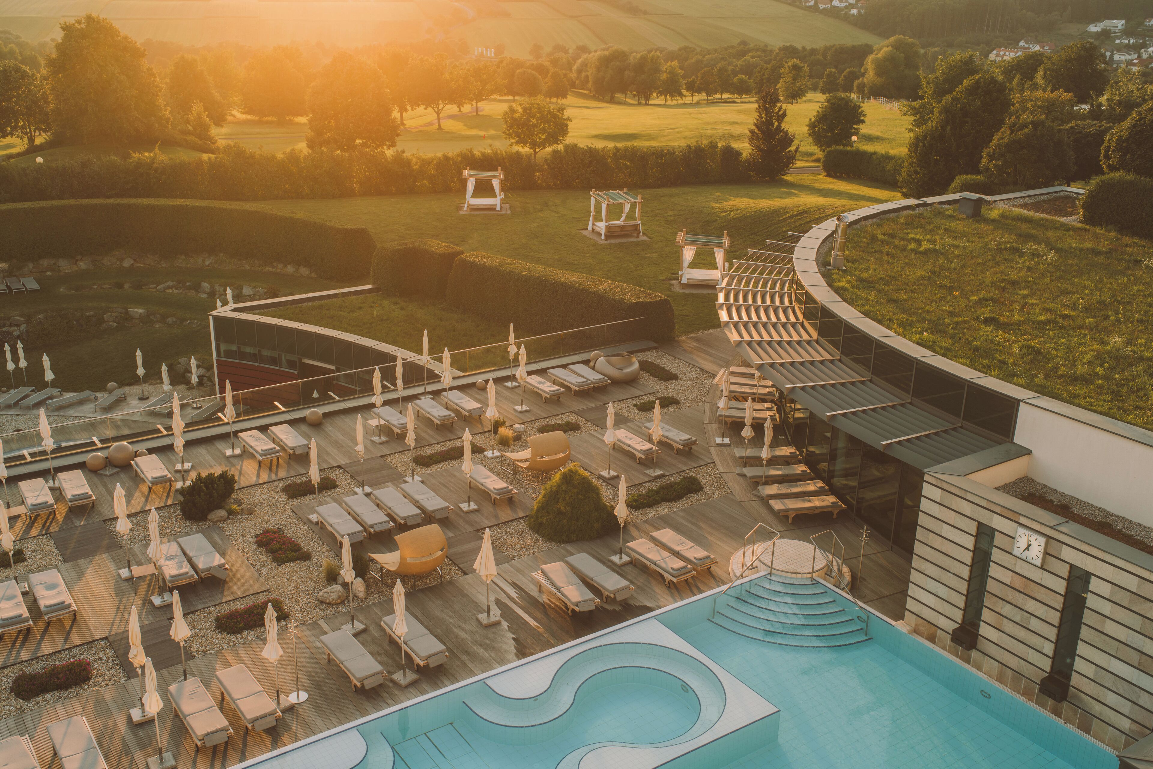Un resort con zona de piscina, tumbonas y un campo de golf al fondo.
