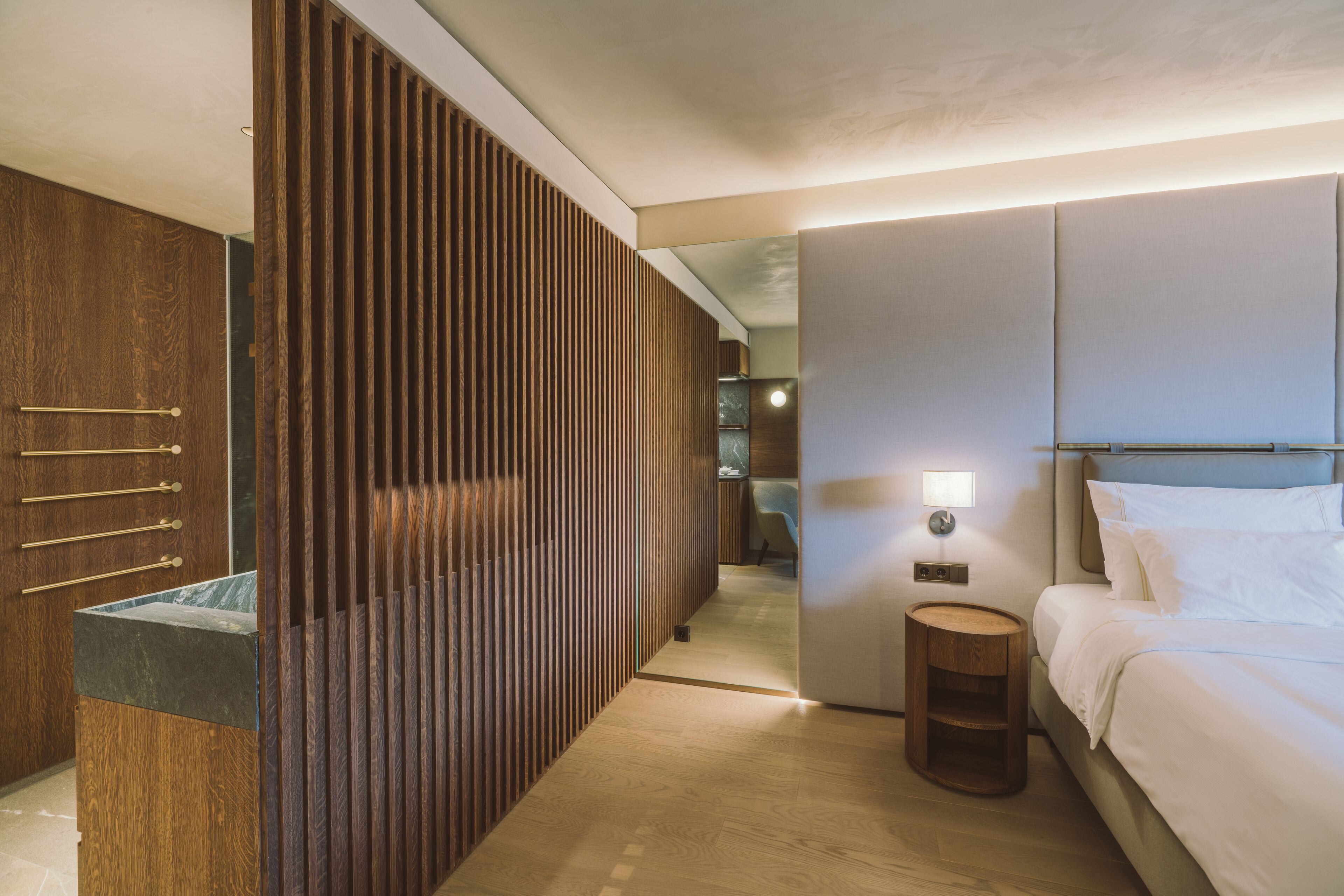 A modern hotel room with a wooden wardrobe, a bedside table, a bed, and a nightstand.