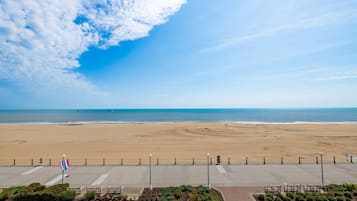A beach view with a clear sky, a flag, and a paved walkway with benches.