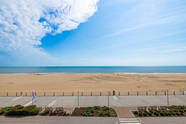Une vue sur la plage, avec un ciel dégagé, un drapeau et une promenade pavée agrémentée de bancs.