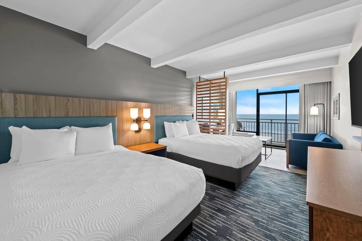Une chambre d’hôtel avec deux lits, un balcon offrant une vue et un bureau avec une chaise.