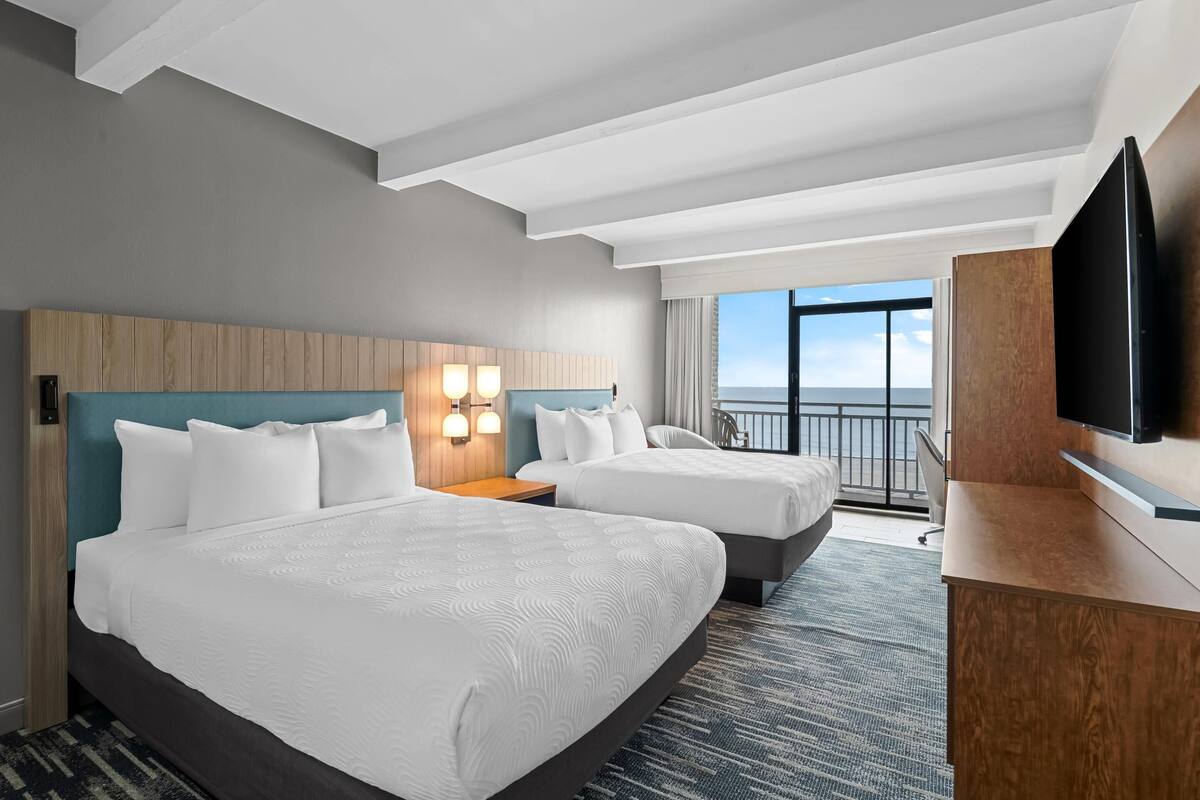 Une chambre d’hôtel avec deux lits, une télévision, un bureau et un balcon avec vue.