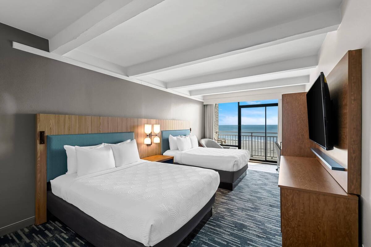Une chambre d’hôtel avec deux lits, une télévision et un balcon donnant sur l’océan.