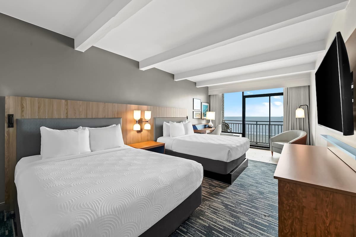 Une chambre d’hôtel avec deux lits, un bureau, une télévision et un balcon avec vue.
