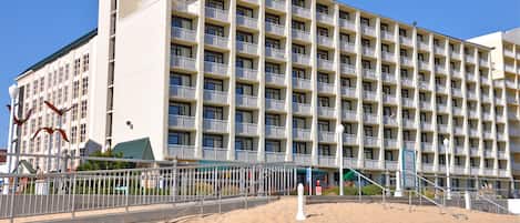 A multi-story hotel with balconies, a sandy beach in front, and a clear blue sky.