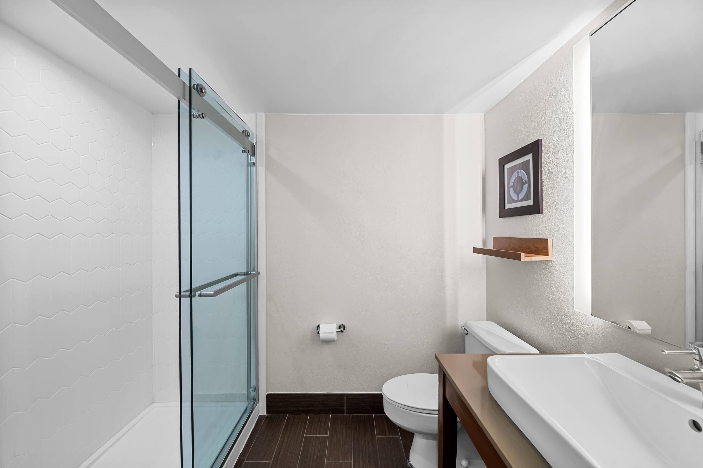 Un baño moderno con cabina de ducha de vidrio, un inodoro blanco y un lavamanos grande y blanco.