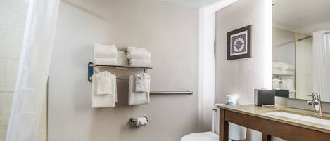 A bathroom with a toilet, sink, and shower area. There are towels hanging on a rack and a framed picture on the wall.