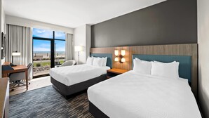 A hotel room with two beds, a desk, and a view of the beach.