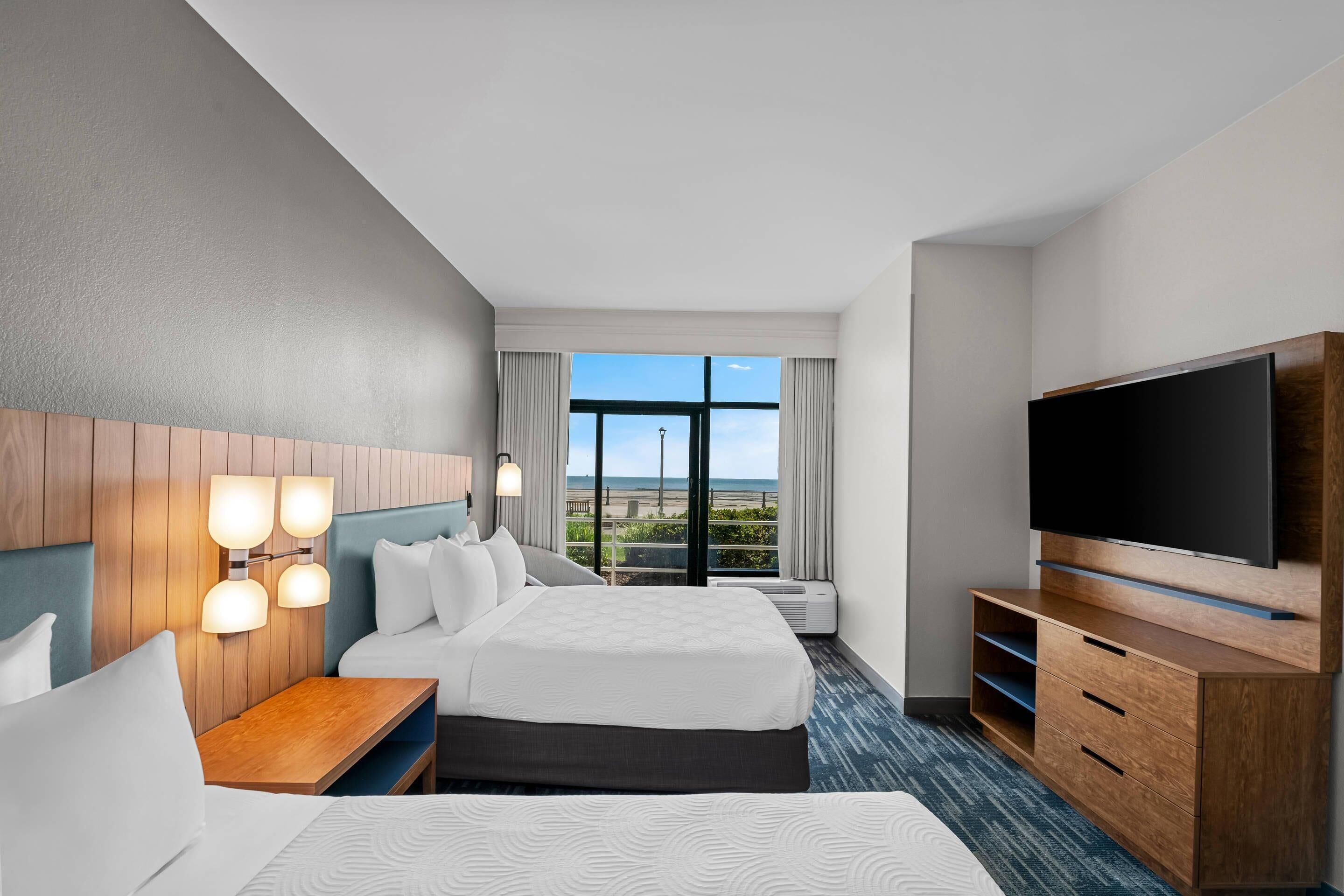A hotel room with two beds, a TV, a desk, and a large window with a view.