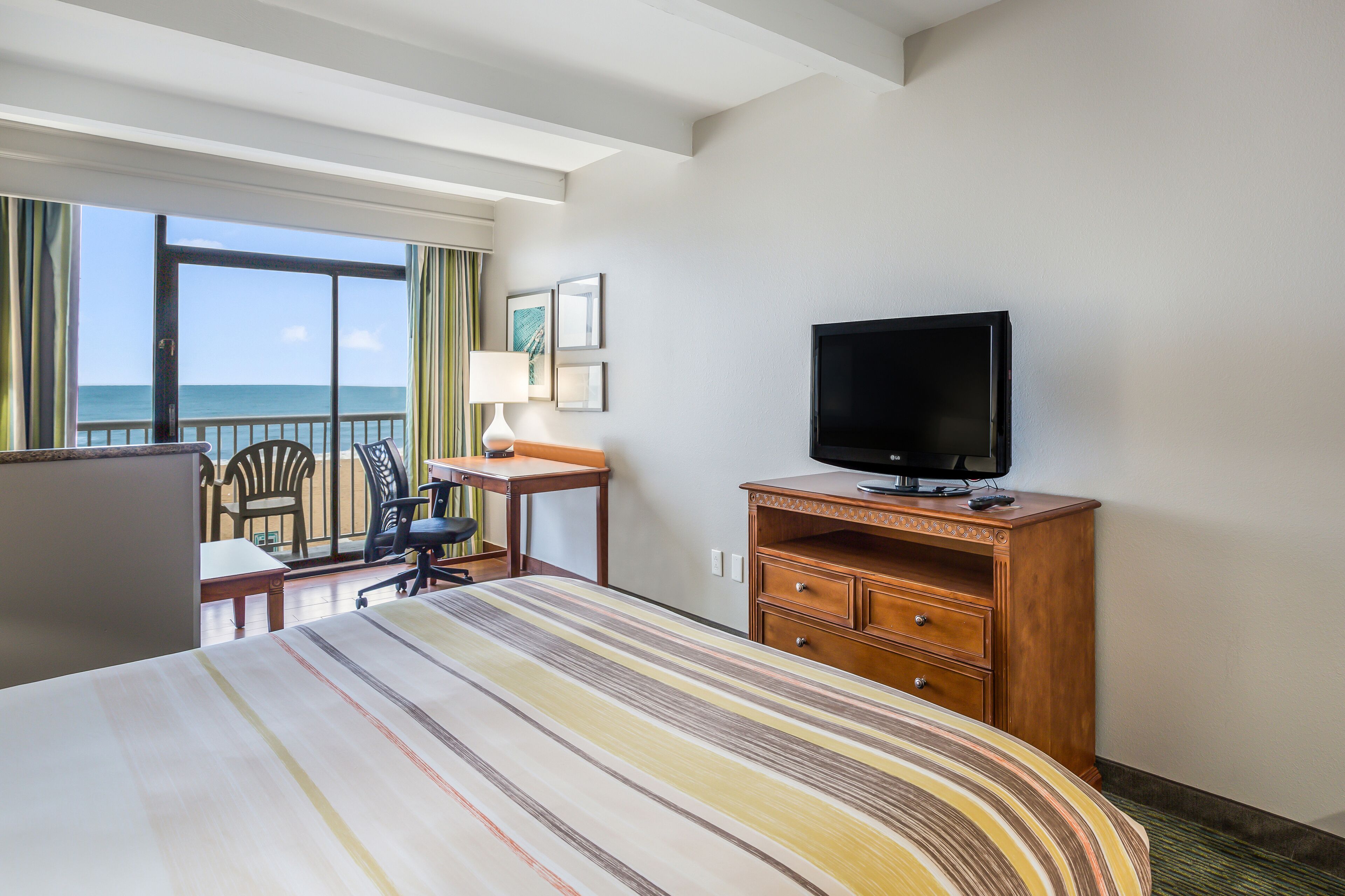 Habitación de hotel con cama, escritorio, televisor y vista al océano.