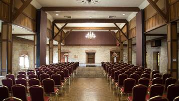 A large hall with rows of red chairs and a stone wall in the background.