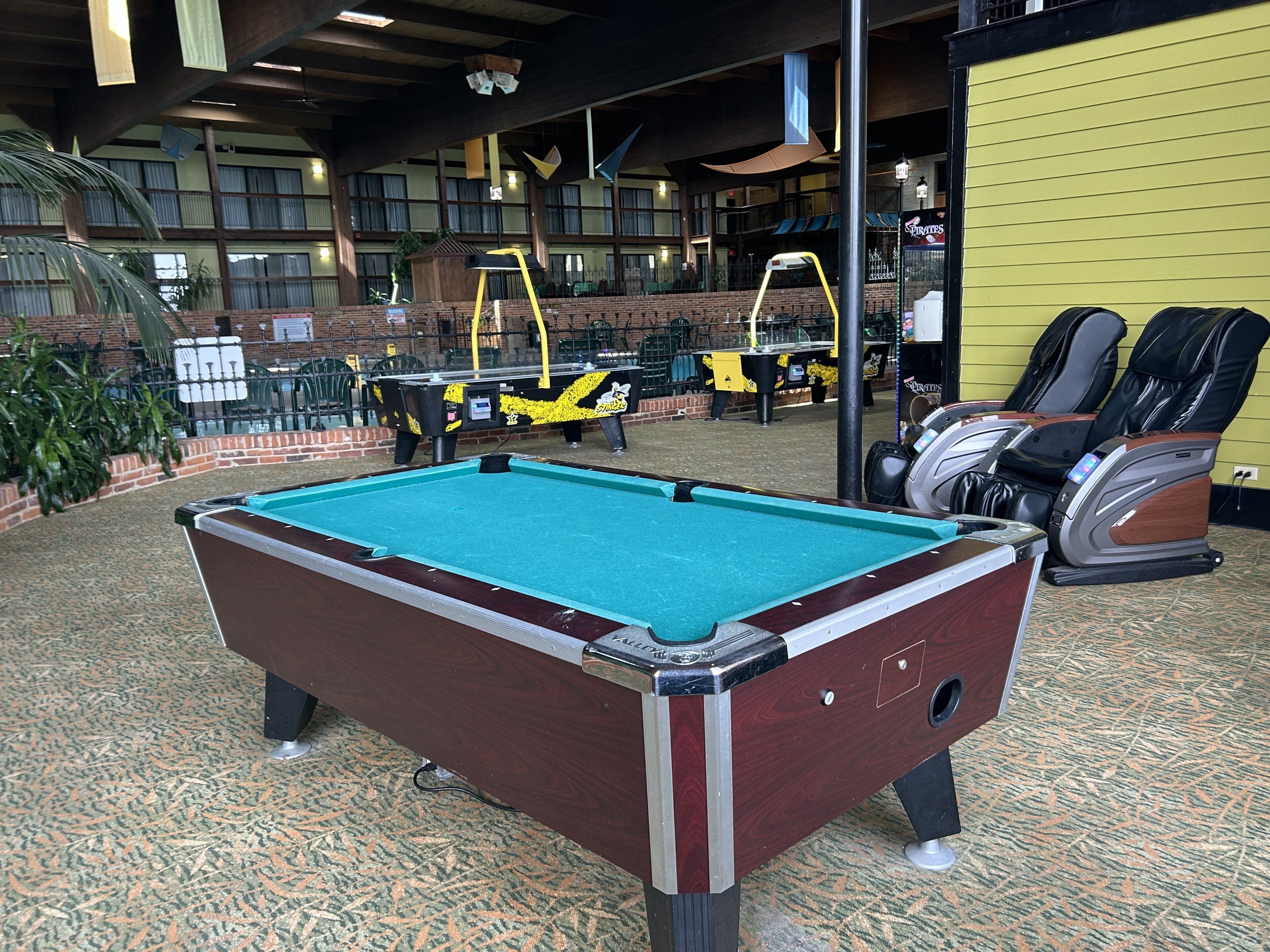 Una mesa de billar en una habitación con vistas a un edificio, una silla de masaje y una mesa de ping pong.