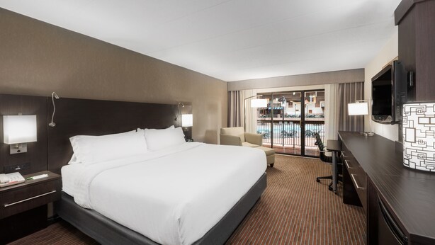 Ein Hotelzimmer mit einem großen Bett, einem Schreibtisch, einem Fernseher und Blick auf einen Pool durch die Glastür.